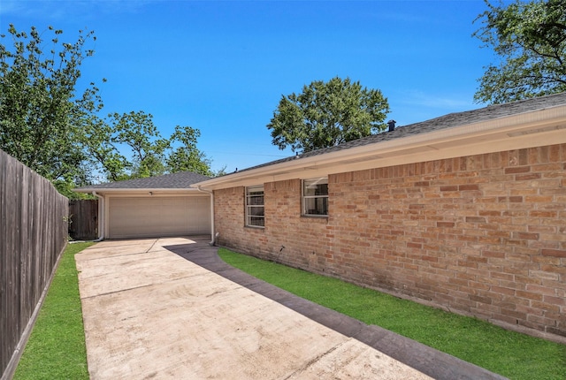 view of side of home featuring fence, concrete driveway, an attached garage, brick siding, and roof with shingles