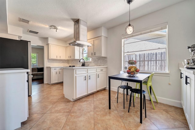 kitchen with island exhaust hood, decorative backsplash, light countertops, freestanding refrigerator, and a textured ceiling