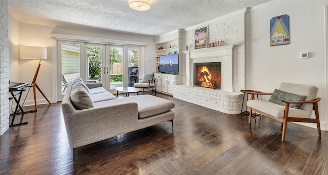 living area with a textured ceiling, a brick fireplace, french doors, dark wood finished floors, and crown molding