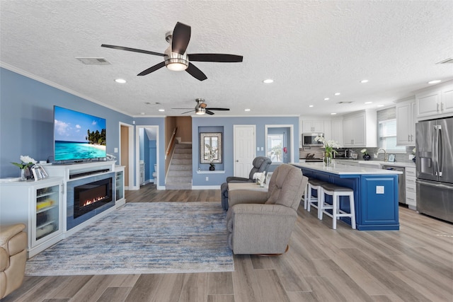 1815 Tiki Dr, Tiki Island, TX 77554 - living room featuring stairway, crown molding, a textured ceiling, ceiling fan, and light wood-style floors