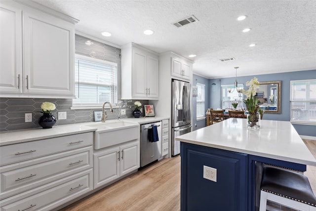 1815 Tiki Dr, Tiki Island, TX 77554 - kitchen featuring appliances with stainless steel finishes, light wood-style flooring, white cabinetry, a textured ceiling, and a breakfast bar area