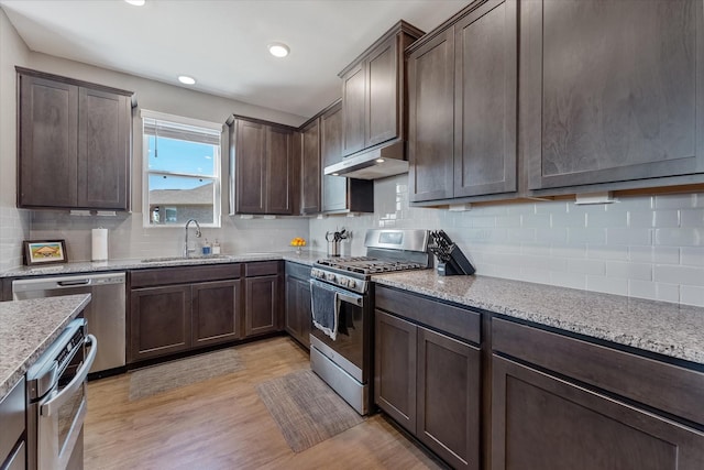 770 Dogberry Ct, Conroe, TX 77304 - kitchen with appliances with stainless steel finishes, a sink, under cabinet range hood, dark brown cabinets, and light wood-style flooring