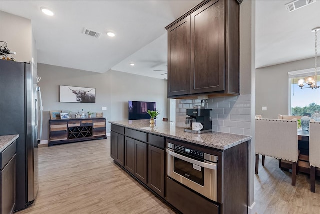 770 Dogberry Ct, Conroe, TX 77304 - kitchen with stainless steel appliances, dark brown cabinets, light wood finished floors, decorative backsplash, and a chandelier