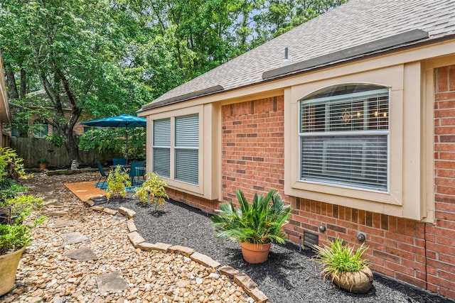 view of home's exterior featuring brick siding, a shingled roof, a patio, and fence
