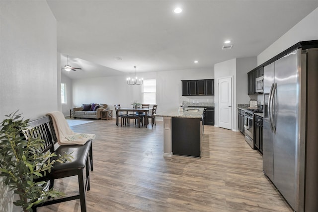 11355 Dawn Beach Ln, Conroe, TX 77304 - kitchen with stainless steel appliances, open floor plan, light stone counters, a center island with sink, and a chandelier