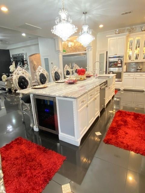 kitchen with appliances with stainless steel finishes, beverage cooler, white cabinets, light stone counters, and recessed lighting