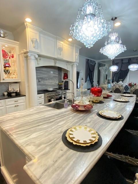 kitchen with a sink, a chandelier, white cabinetry, a breakfast bar, and light countertops