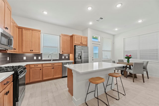 21106 Garden Palm Dr, Cypress, TX 77433 - kitchen with stainless steel appliances, a breakfast bar area, a sink, decorative backsplash, and light wood finished floors