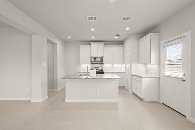 2906 Park Hill Ln, Stafford, TX 77477 - kitchen featuring appliances with stainless steel finishes, white cabinets, light stone counters, a center island with sink, and recessed lighting