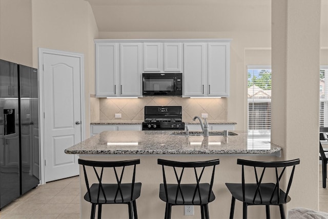 635 W Linnwood Dr, Woodbranch, TX 77357 - kitchen featuring black appliances, white cabinetry, backsplash, and light stone counters