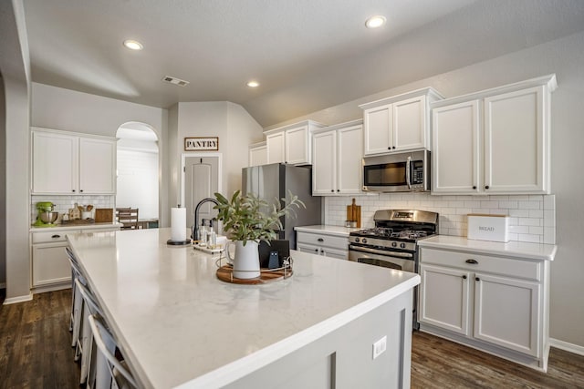 123 Clearmont Pl, Montgomery, TX 77316 - kitchen with appliances with stainless steel finishes, decorative backsplash, white cabinetry, a kitchen island with sink, and dark wood finished floors