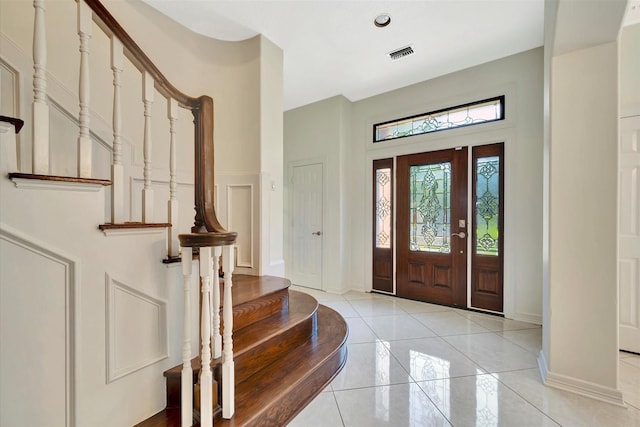 foyer entrance with stairway, baseboards, a decorative wall, and light tile patterned floors