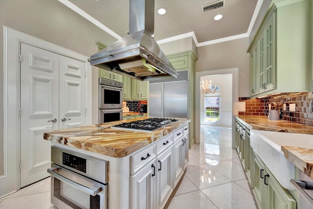 kitchen featuring green cabinetry, stainless steel appliances, island range hood, ornamental molding, and decorative backsplash