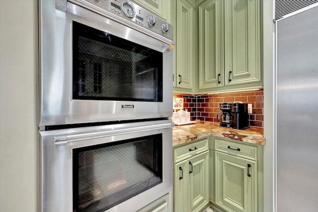 kitchen featuring green cabinetry, stainless steel appliances, light countertops, and tasteful backsplash
