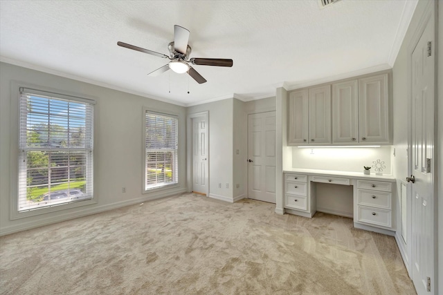 unfurnished bedroom featuring crown molding, light colored carpet, baseboards, an office area, and a ceiling fan