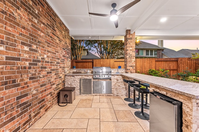 view of patio / terrace featuring grilling area, an outdoor kitchen, a fenced backyard, and a ceiling fan
