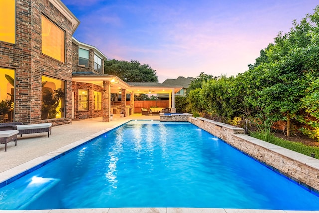 pool at dusk featuring an outdoor pool, a patio area, outdoor lounge area, and an in-ground hot tub