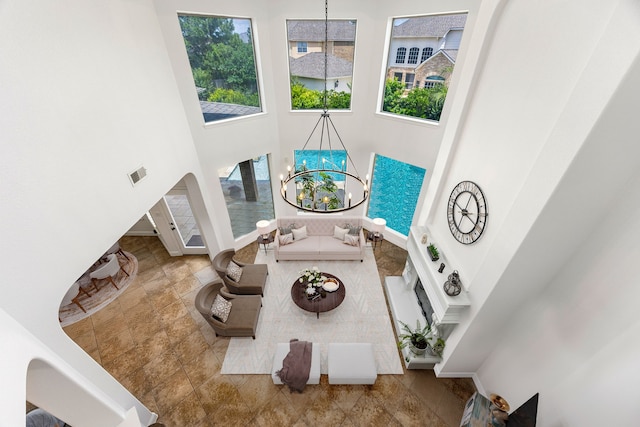 living room featuring healthy amount of natural light, a high ceiling, a chandelier, stone finish flooring, and baseboards