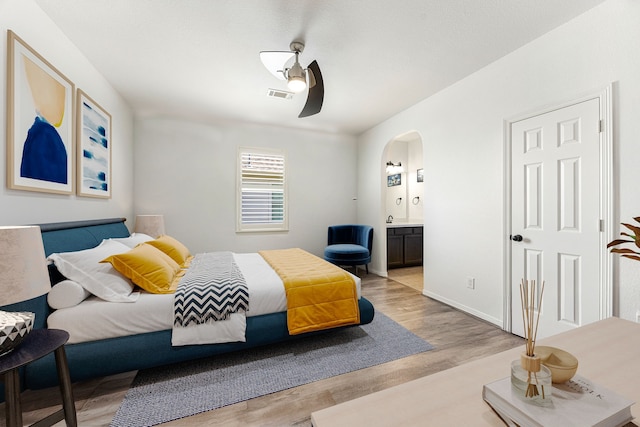 bedroom featuring light wood-type flooring, arched walkways, ensuite bathroom, and baseboards