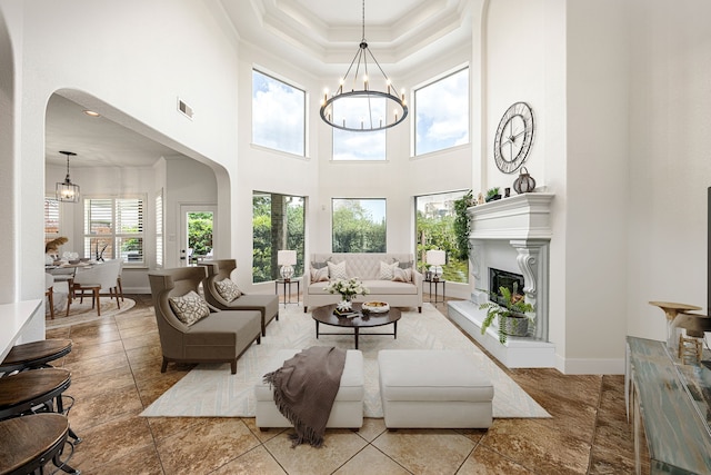 living room with a high ceiling, a chandelier, arched walkways, crown molding, and a glass covered fireplace