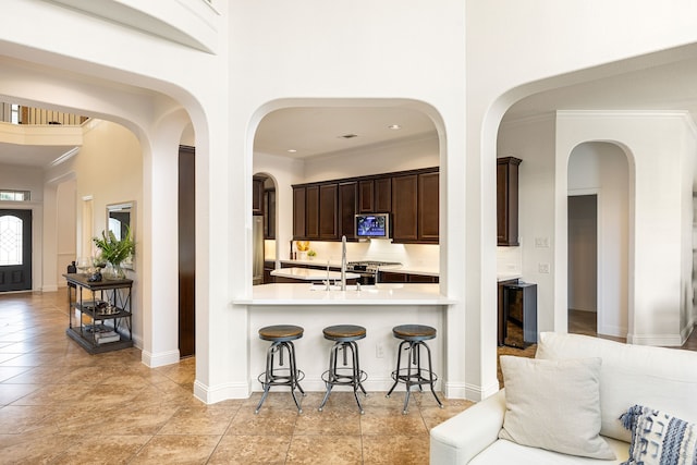 kitchen featuring stainless steel appliances, a breakfast bar, dark brown cabinetry, beverage cooler, and a towering ceiling