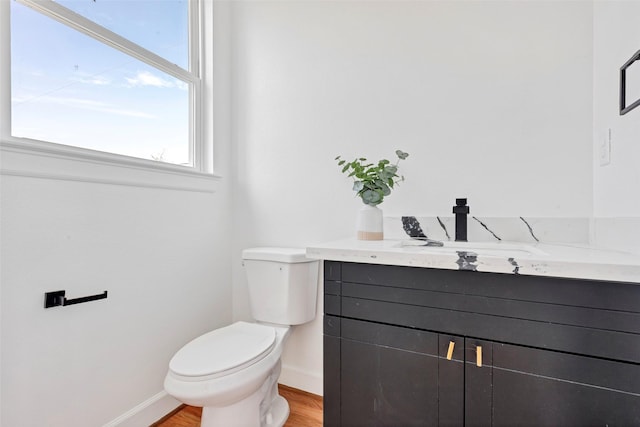 bathroom featuring baseboards, toilet, wood finished floors, and vanity