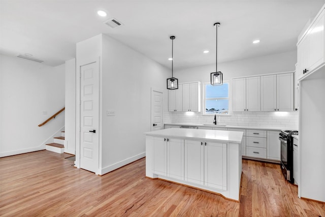 kitchen with black gas stove, a center island, light wood-style floors, decorative backsplash, and light countertops