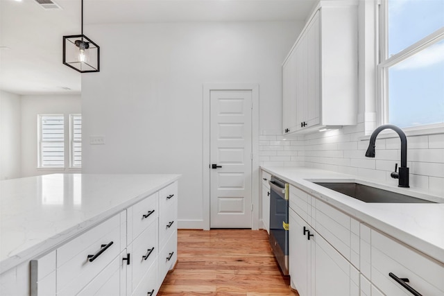 kitchen featuring a sink, backsplash, light wood-style flooring, light stone counters, and white cabinets