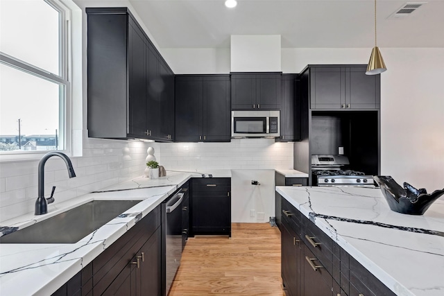 kitchen with stainless steel appliances, a sink, light stone countertops, and dark cabinets
