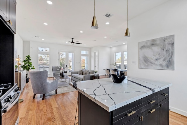 kitchen with stainless steel gas range, light wood-style flooring, dark cabinets, recessed lighting, and a center island