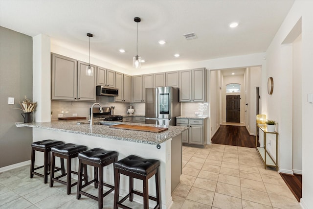 kitchen featuring stainless steel appliances, gray cabinets, a peninsula, decorative backsplash, and baseboards