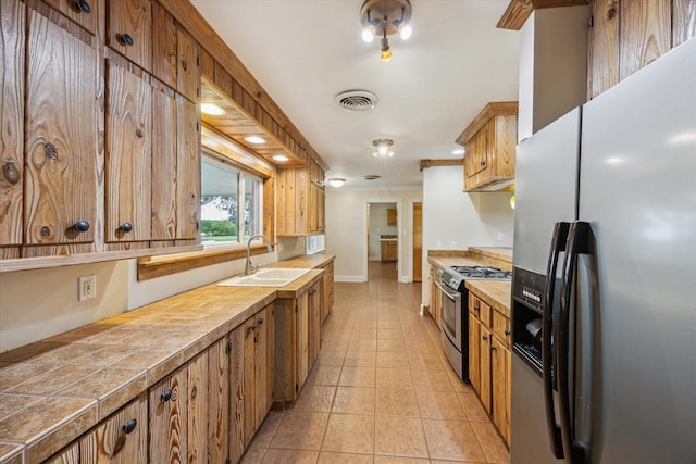 13016 W Burton St, Burton, TX 77835 - kitchen with appliances with stainless steel finishes, a sink, brown cabinets, tile countertops, and light tile patterned floors
