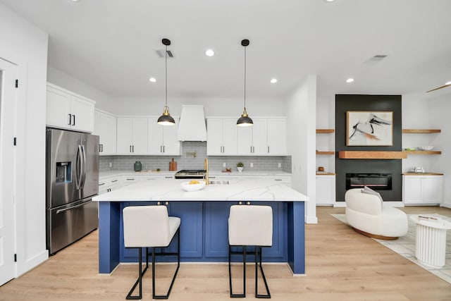5520 Chapman St, Houston, TX 77009 - kitchen with stainless steel refrigerator with ice dispenser, custom range hood, light wood-type flooring, backsplash, and light stone countertops