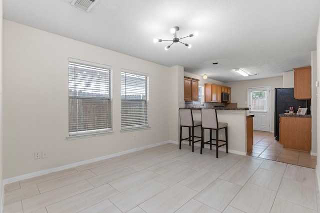 14502 Windmill Meadows Ct, Houston, TX 77082 - kitchen with a peninsula, a chandelier, a breakfast bar, brown cabinetry, and tasteful backsplash