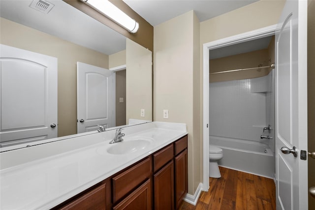 bathroom featuring toilet, wood finished floors, vanity, and shower / washtub combination