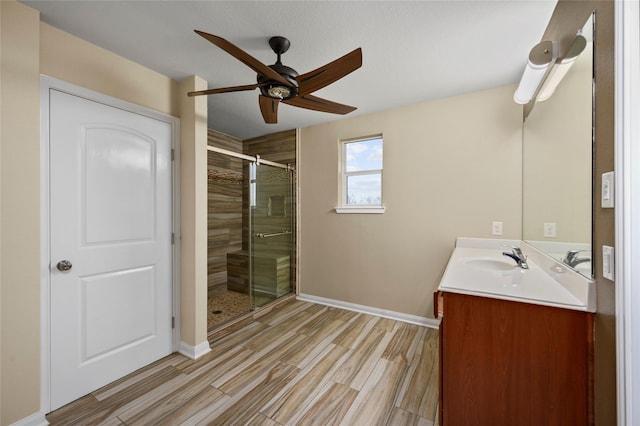 bathroom with ceiling fan, a stall shower, vanity, wood finished floors, and baseboards