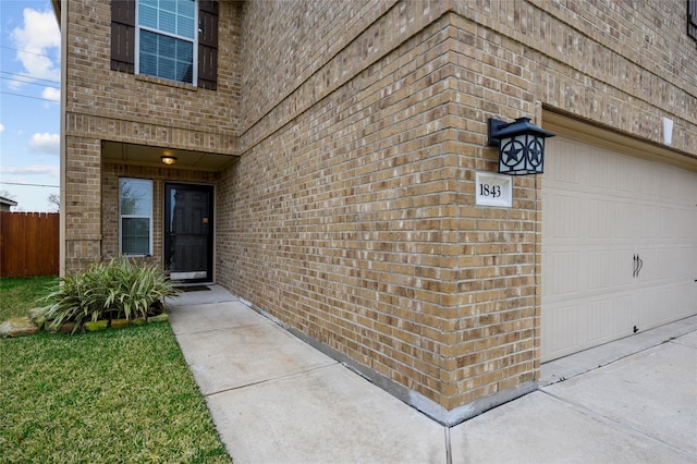 view of exterior entry featuring brick siding, fence, and a garage