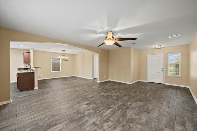 unfurnished living room featuring dark wood finished floors, ceiling fan, arched walkways, and baseboards