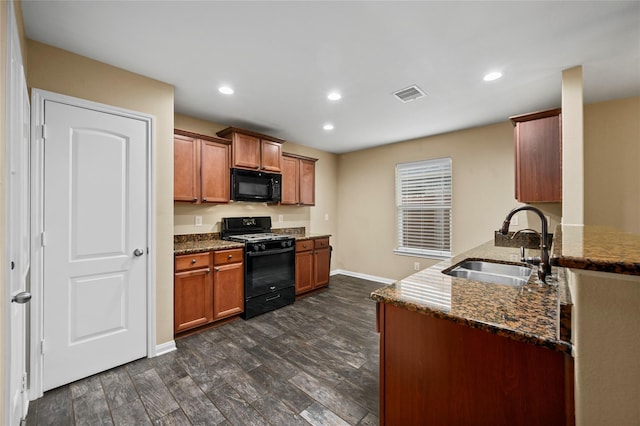 kitchen with range with gas stovetop, black microwave, a sink, dark stone countertops, and baseboards