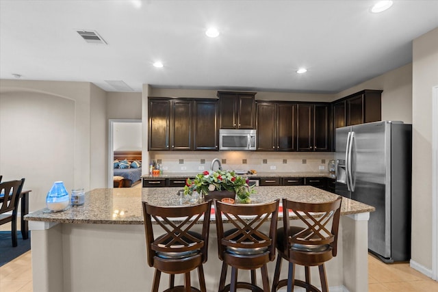 4603 Tamara Heights Ln, Sugar Land, TX 77479 - kitchen with stainless steel appliances, dark brown cabinetry, an island with sink, light stone countertops, and decorative backsplash