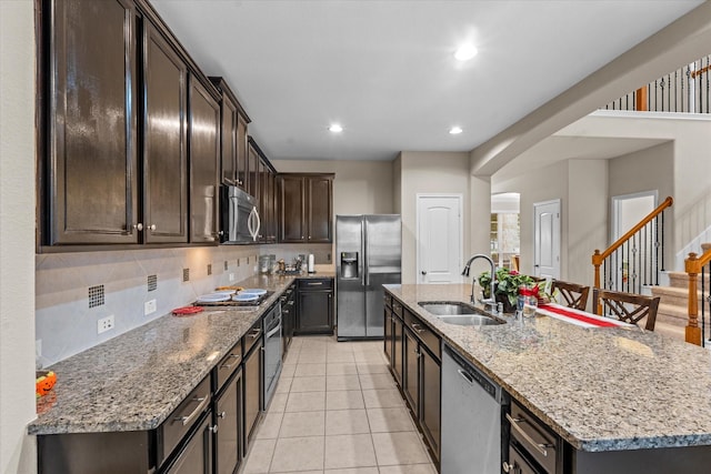 4603 Tamara Heights Ln, Sugar Land, TX 77479 - kitchen with stainless steel appliances, a sink, dark brown cabinets, a center island with sink, and light stone counters