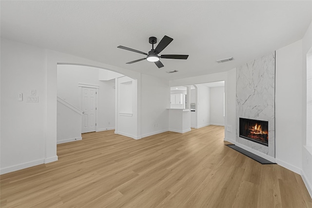 unfurnished living room featuring ceiling fan, light wood-style flooring, a premium fireplace, arched walkways, and baseboards