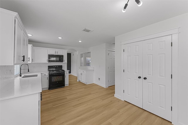 kitchen with black appliances, a sink, light wood-type flooring, white cabinets, and light countertops