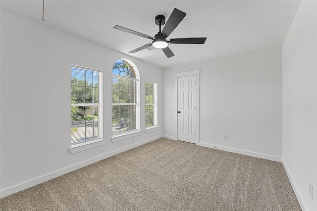 carpeted spare room featuring baseboards and a ceiling fan