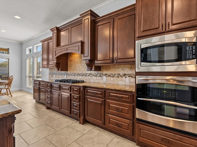 913 Ember Hills Ln, Friendswood, TX 77546 - kitchen with stainless steel appliances, crown molding, backsplash, light tile patterned flooring, and light stone counters