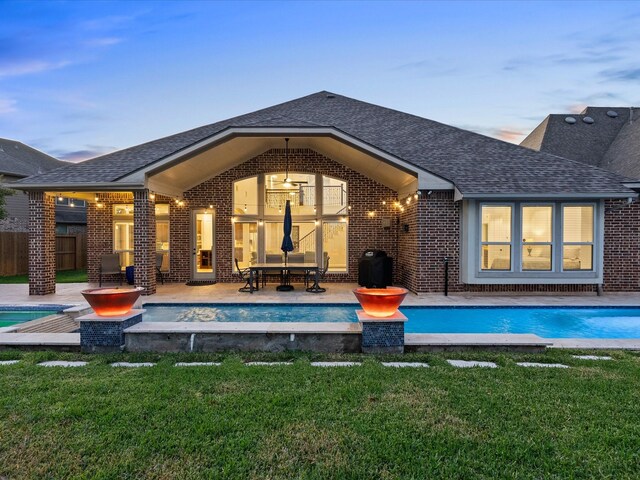 913 Ember Hills Ln, Friendswood, TX 77546 - back of house at dusk with roof with shingles, brick siding, an outdoor pool, and a patio area