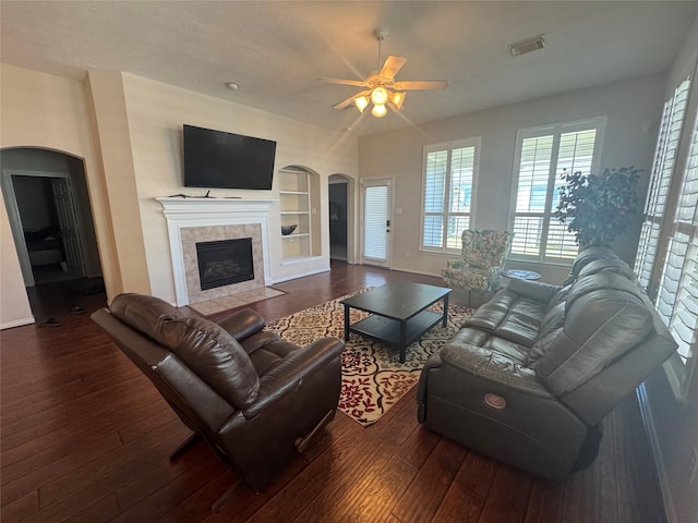 living room with arched walkways, a ceiling fan, wood-type flooring, and built in shelves