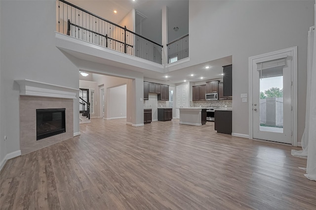 707 Fresh Sage Xing, Richmond, TX 77406 - unfurnished living room featuring light wood-style floors, a high ceiling, a fireplace, baseboards, and stairs