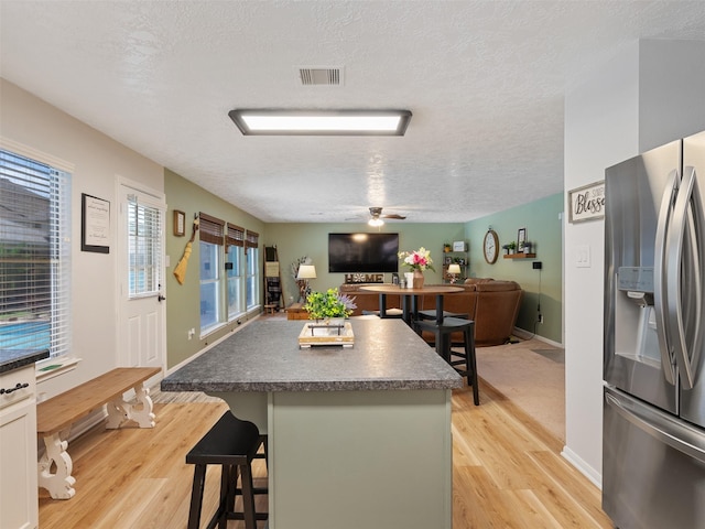 11823 Elizabeth Ct, Pinehurst, TX 77362 - kitchen with stainless steel fridge, a textured ceiling, a center island, light wood-style flooring, and a kitchen breakfast bar