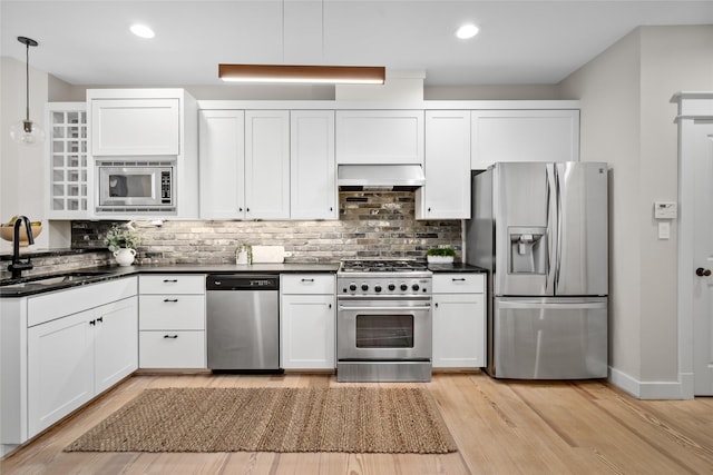1728 Nicholson St, Houston, TX 77008 - kitchen featuring stainless steel appliances, a sink, dark countertops, wall chimney range hood, and white cabinetry